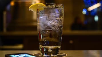 Un vaso de agua con hielo y una rodaja de limón sobre un posavasos, con un teléfono inteligente sobre la mesa.