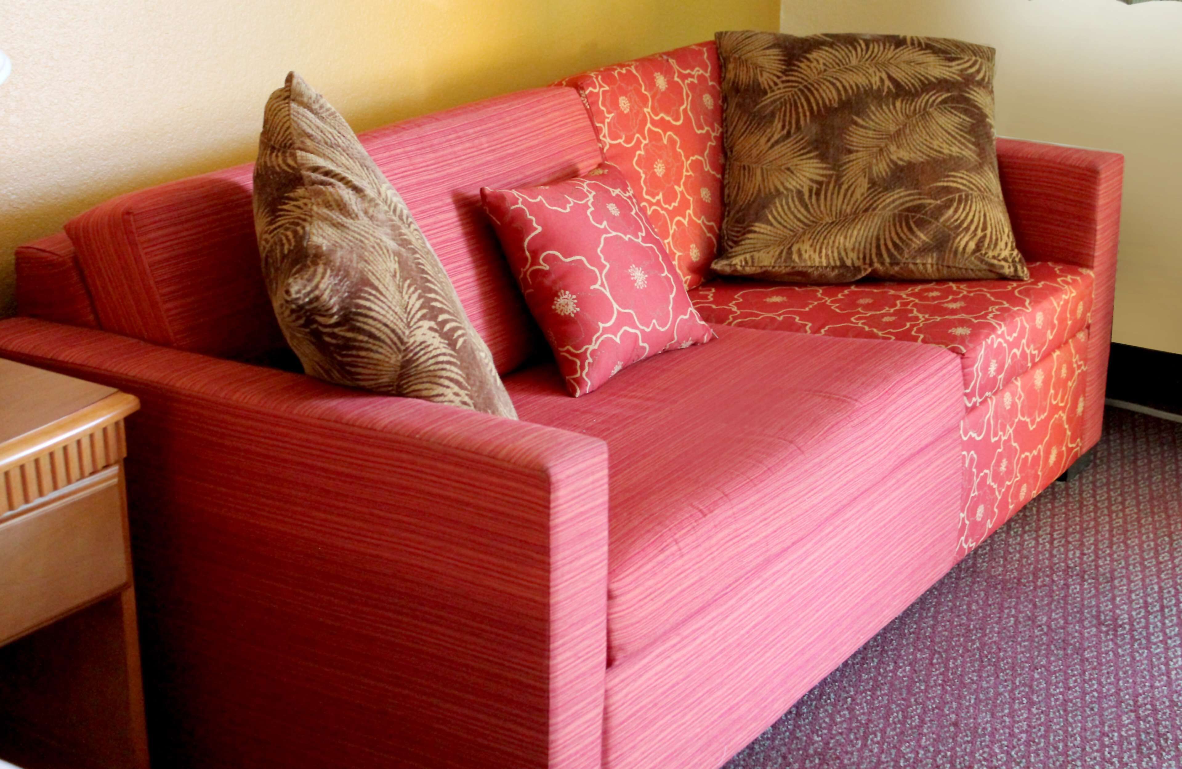 Un sofá rojo con cojines estampados en una habitación con una mesita de madera y una alfombra con motivos.