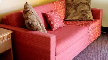 Un sofá rojo con cojines estampados en una habitación con una mesita de madera y una alfombra con motivos.