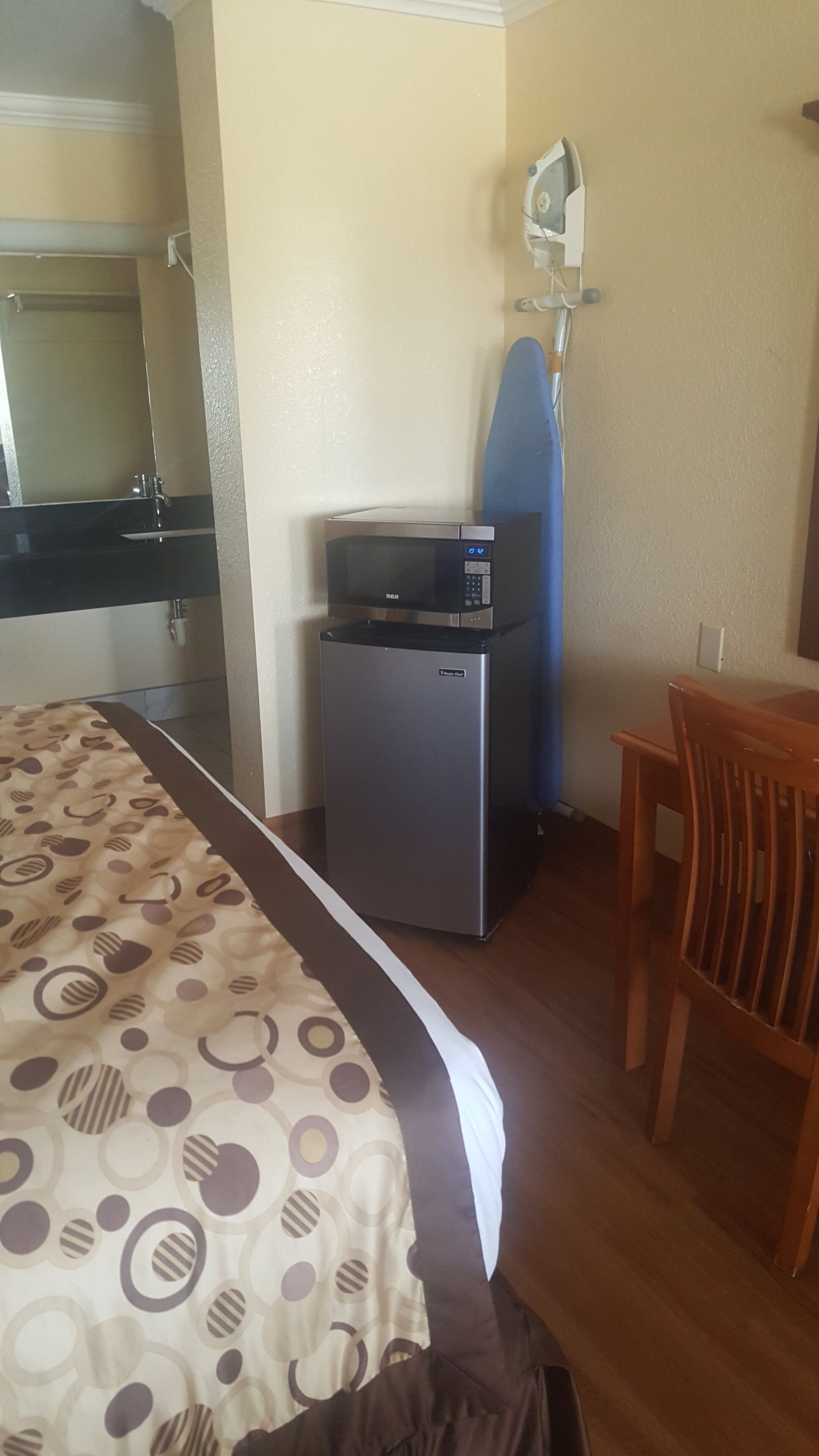 Una habitación de hotel con cama, refrigerador pequeño, microondas, mesa y silla.