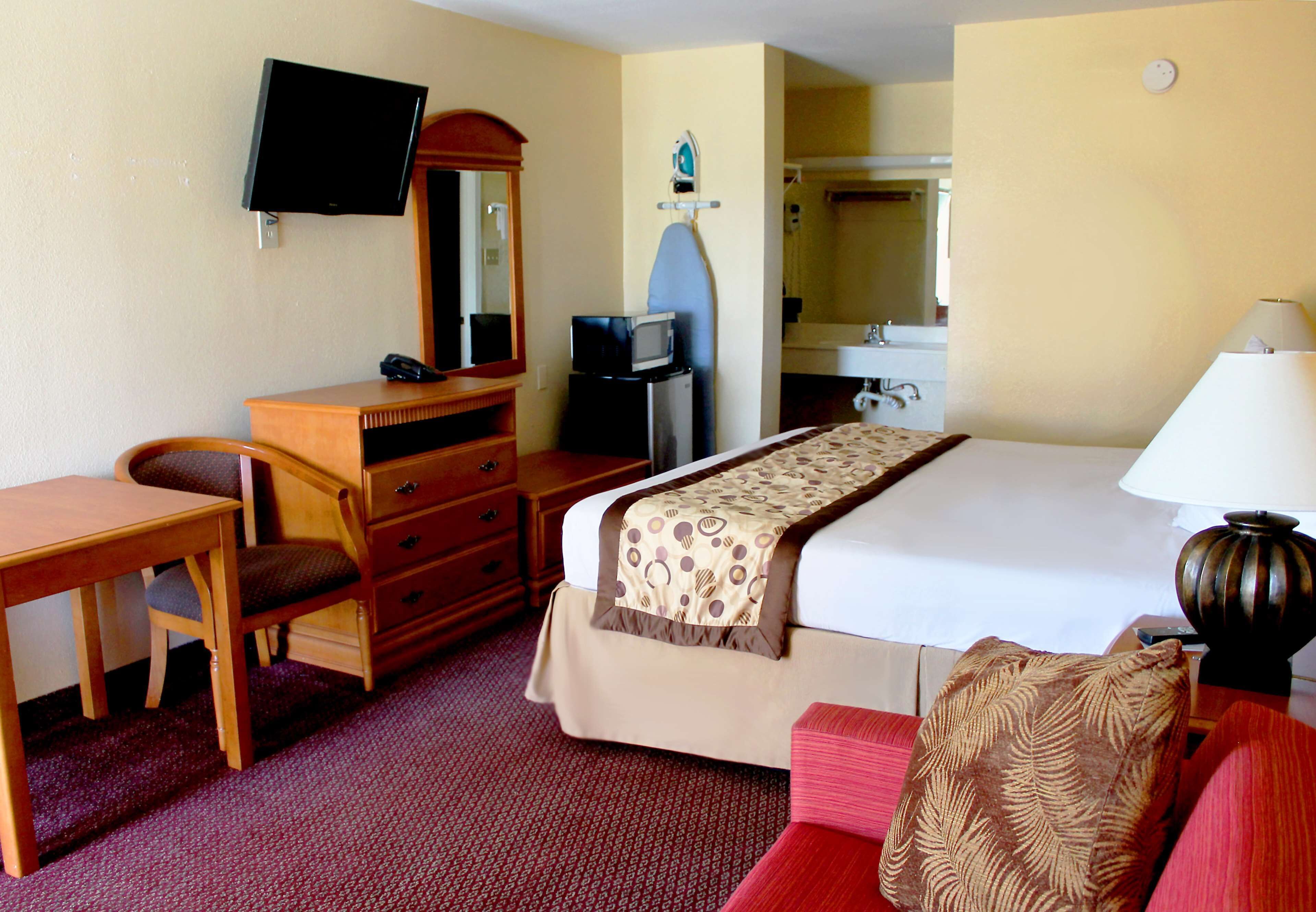 A hotel room with a bed, a desk, a chair, a television, a microwave, a dresser, and a bathroom visible through an open door.