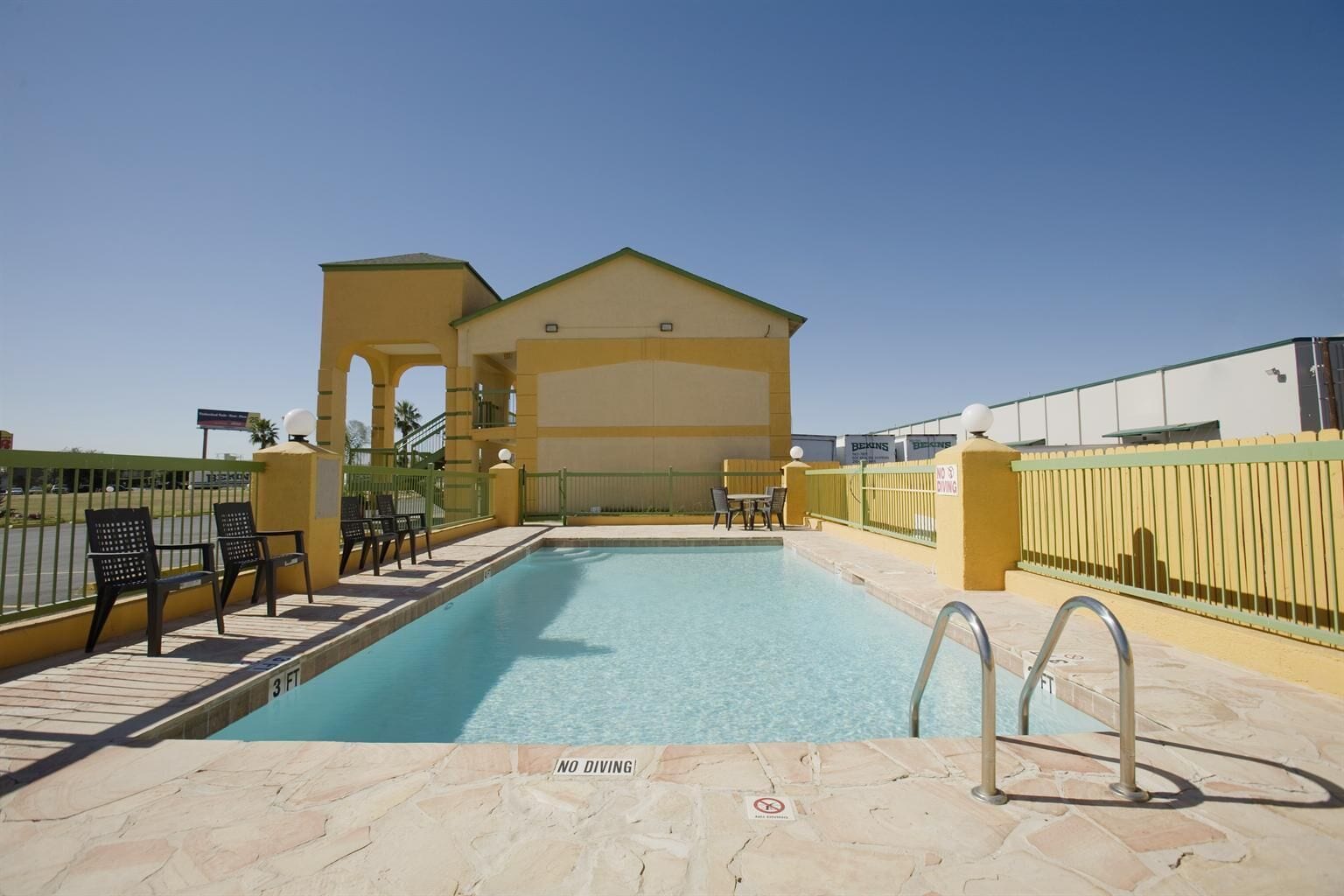 A swimming pool with a 'No Diving' sign, a covered seating area, and a building with a yellow facade.