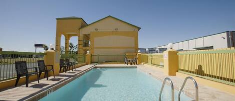 A swimming pool with a 'No Diving' sign, a covered seating area, and a building with a yellow facade.