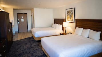 A hotel room with two beds, a wooden headboard, a nightstand with a lamp, a framed picture on the wall, and a door leading to another room.