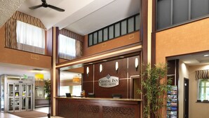 Zona de recepción de hotel con un cartel que indica Crystal Inn Hotel Suites, un mostrador de recepción, una caja registradora, una planta y una puerta giratoria.
