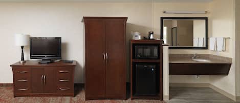 Habitación de hotel con armario de madera, televisor, microondas y lavamanos con espejo.