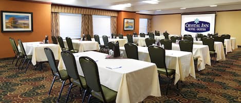 A conference room with multiple tables and chairs, a carpeted floor, and a presentation screen displaying the hotel name.