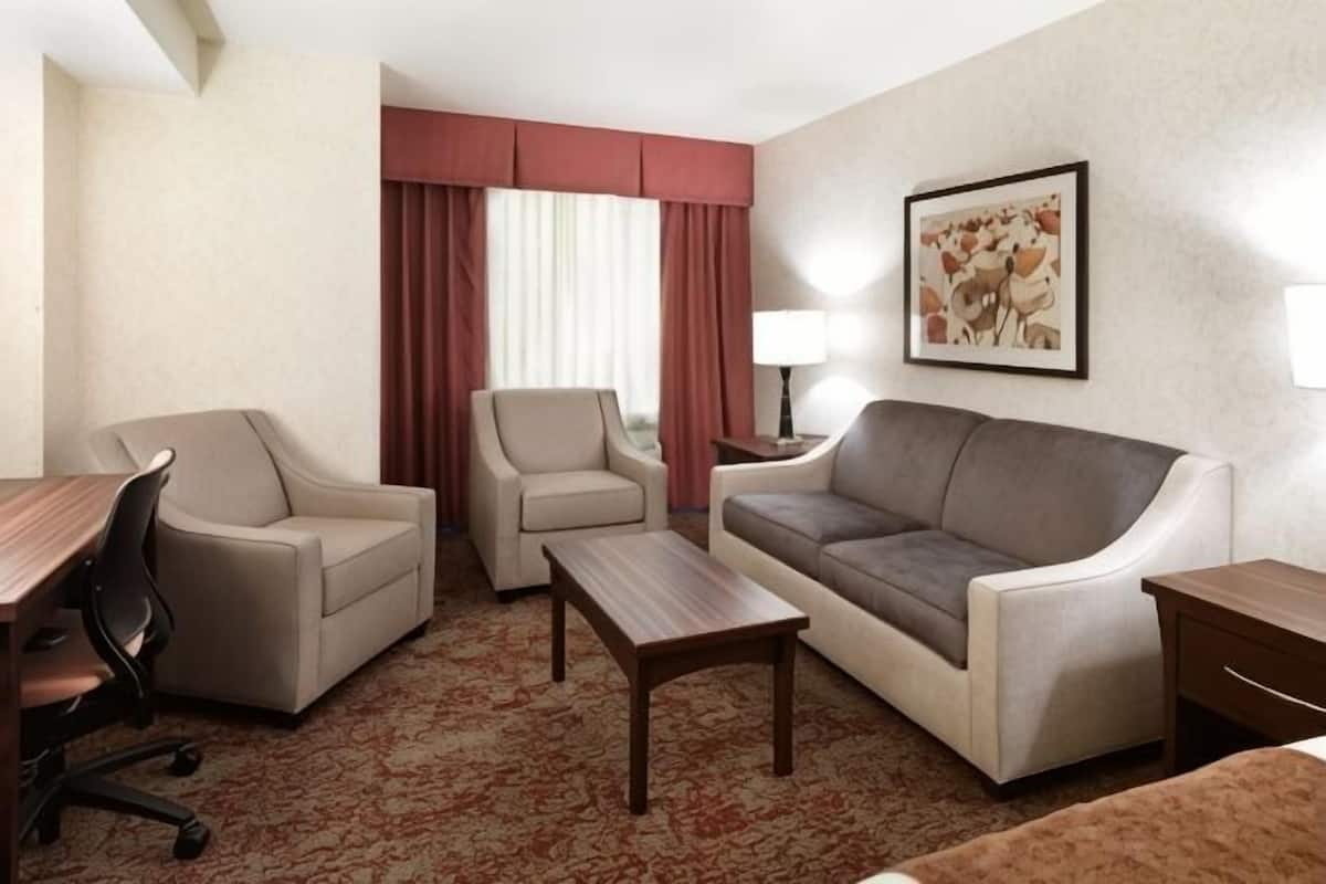 A hotel room with a sofa, two armchairs, a desk, a lamp, and a framed picture on the wall.