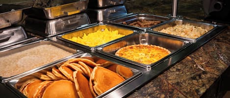 A buffet with various food items including pancakes, potatoes, and a pie.