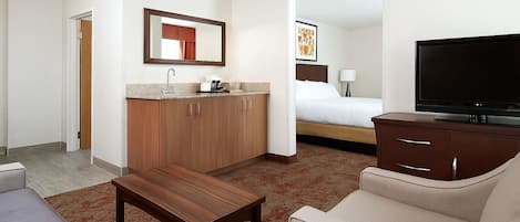 A hotel room with a bed, a TV, a sofa, a coffee table, a desk, and a bathroom visible through an open door.