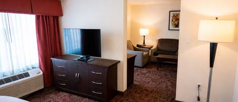 Una habitación de hotel con una cama, un televisor en una cómoda, un escritorio con una lámpara y una silla.
