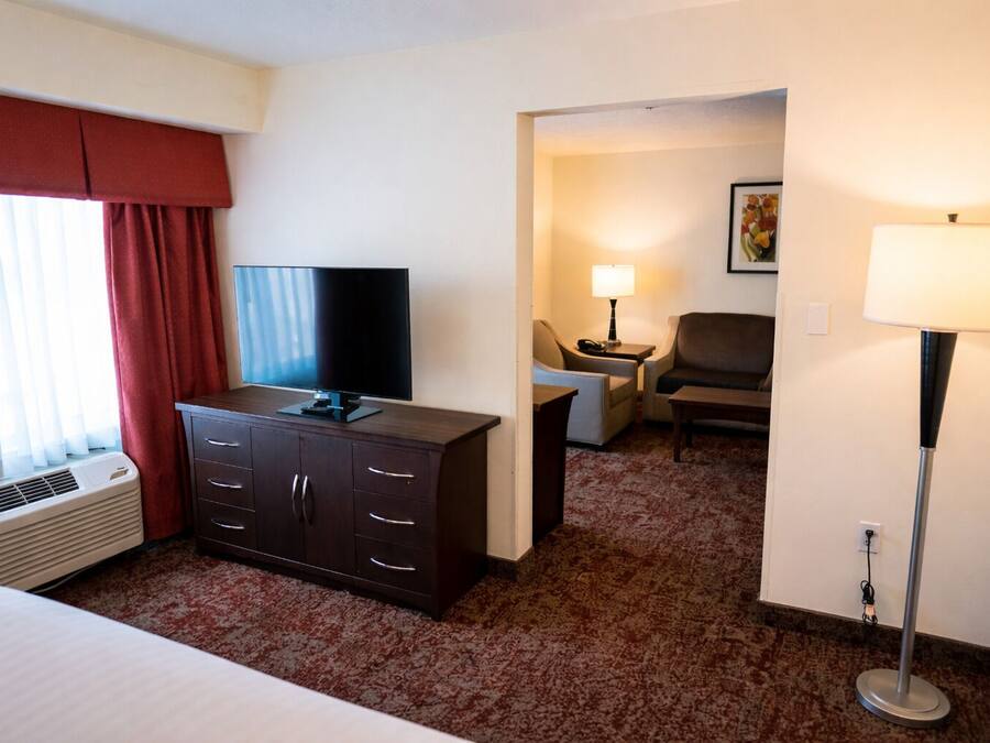 A hotel room with a bed, a TV on a dresser, a desk with a lamp, and a chair.