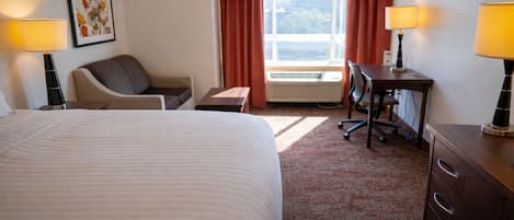 A hotel room with a large bed, a desk with a chair, a small table, and two lamps.