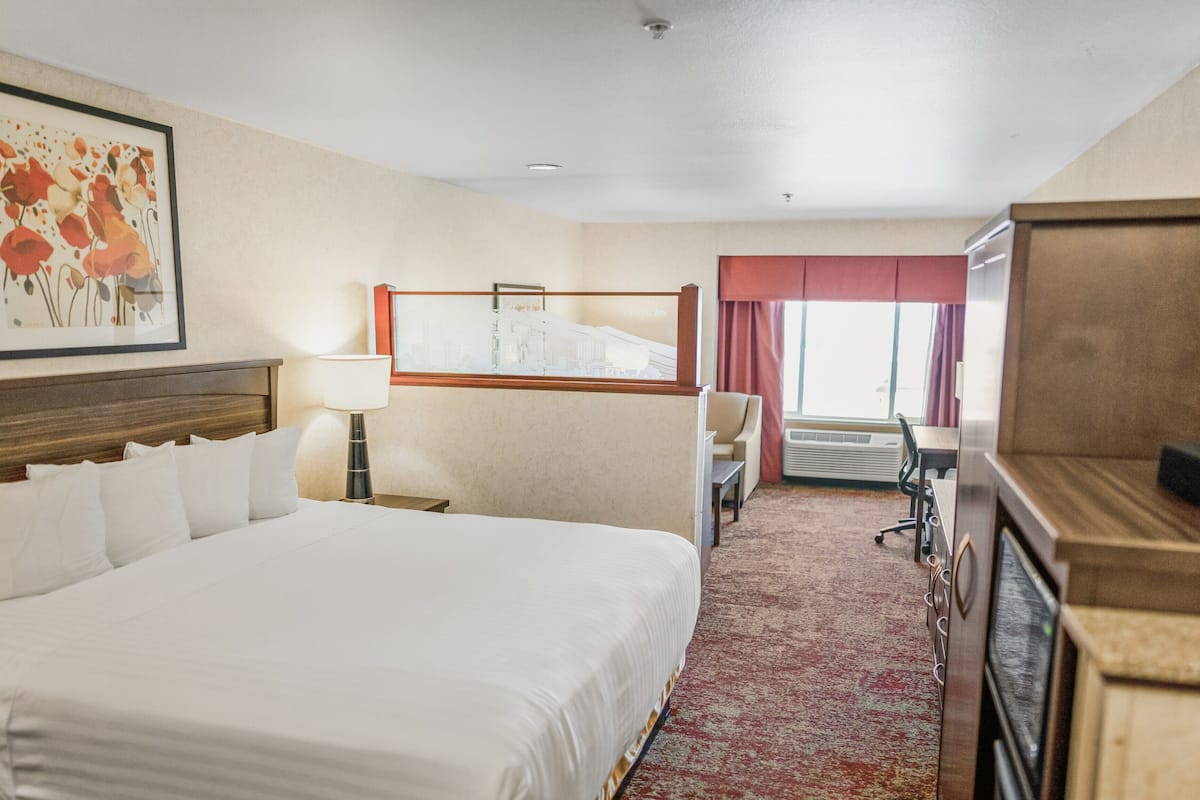 A hotel room with a large bed, a desk, a chair, a lamp, and a window with curtains.