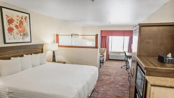 Une chambre d’hôtel avec un grand lit, un bureau, une chaise, une lampe et une fenêtre avec des rideaux.