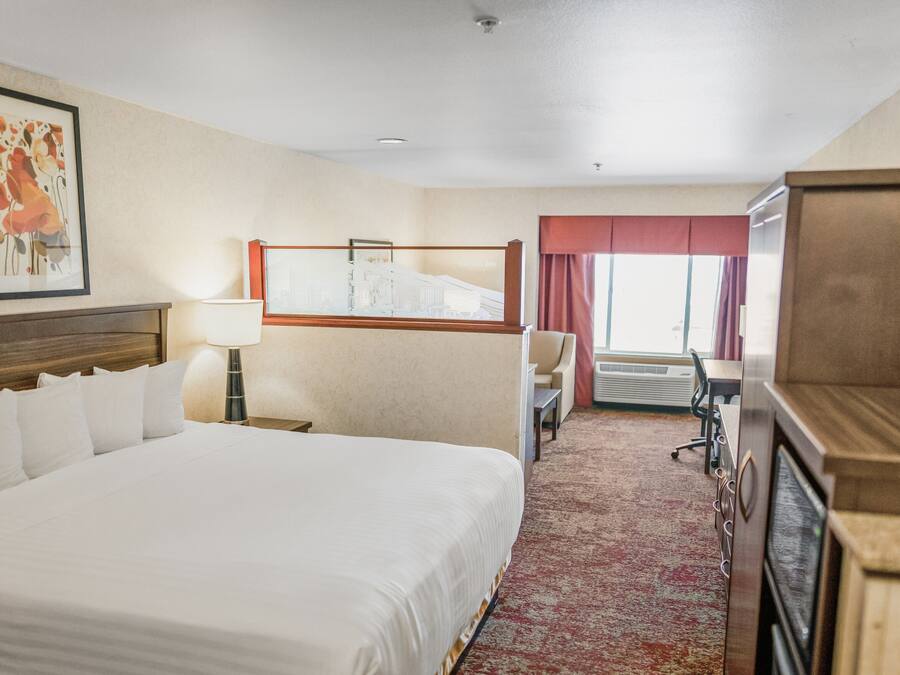 Une chambre d’hôtel avec un grand lit, un bureau, une chaise, une lampe et une fenêtre avec des rideaux.