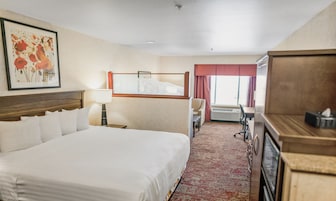 Habitación de hotel con una cama grande, un escritorio, una silla, una lámpara y una ventana con cortinas.