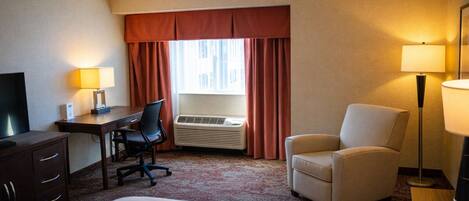A hotel room with a bed, a desk, a chair, a TV, an air conditioner, and a lamp.
