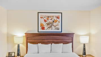 Habitación de hotel con una cama grande, dos mesitas de noche con lámparas, una obra enmarcada sobre la cama y un teléfono en la mesita de la izquierda.