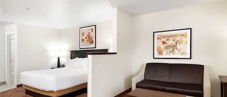 Habitación de hotel con cama, sofá, una pequeña mesa y dos cuadros enmarcados en las paredes.
