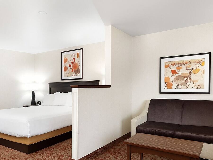 A hotel room with a bed, a sofa, a small table, and two framed artworks on the walls.