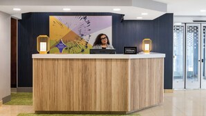 A hotel reception desk with a wooden finish, a large abstract painting, and two illuminated wall sconces. - Spark by Hilton Salt Lake City Airport (Salt Lake City)