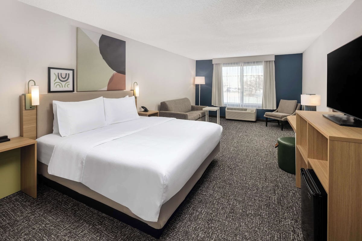 A hotel room with a large bed, two armchairs, a small table, a TV, and a desk with a lamp.