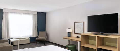 A hotel room with a bed, a desk, a chair, a television, and a small refrigerator.