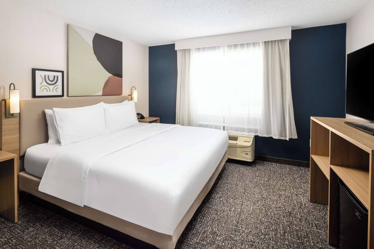 A hotel room with a large bed, a flat-screen TV, a desk, and a window with curtains.