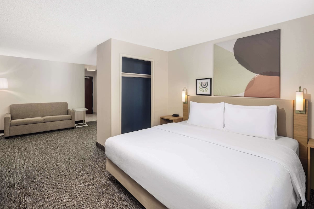 A hotel room with a large bed, a sofa, a desk, and a door.