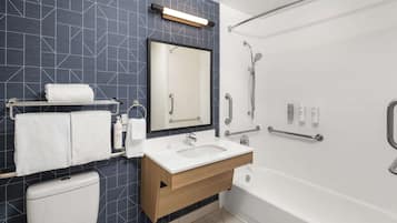 A modern bathroom with a dark tiled wall, a white sink, a mirror, a toilet, and a shower area.