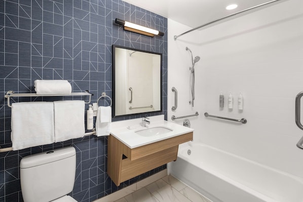 A modern bathroom with a dark tiled wall, a white sink, a mirror, a toilet, and a shower area.