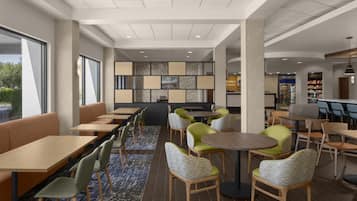 A modern indoor seating area with tables and chairs, a patterned wall, and a reception desk.