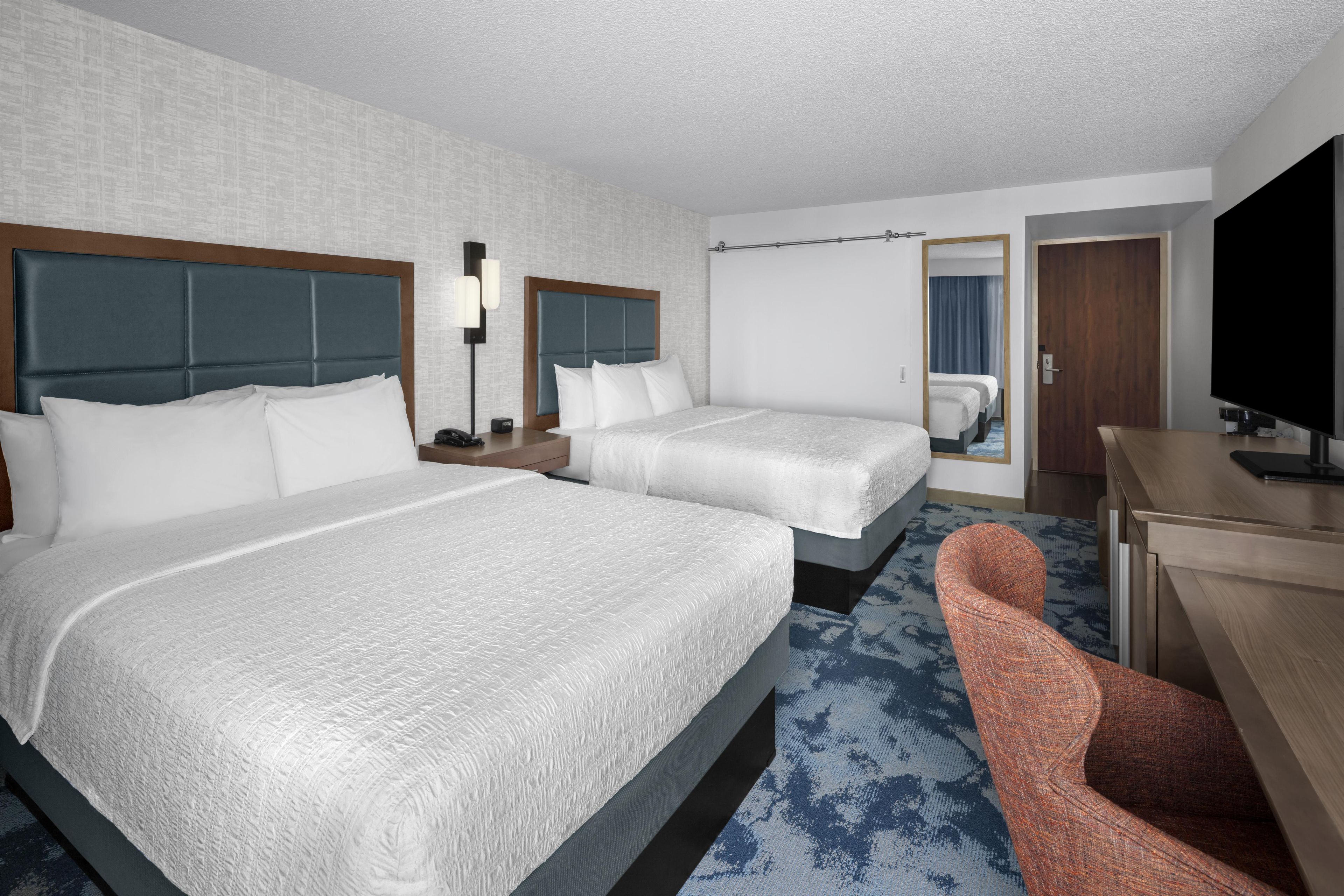 A hotel room with two beds, a desk, a TV, and a chair.