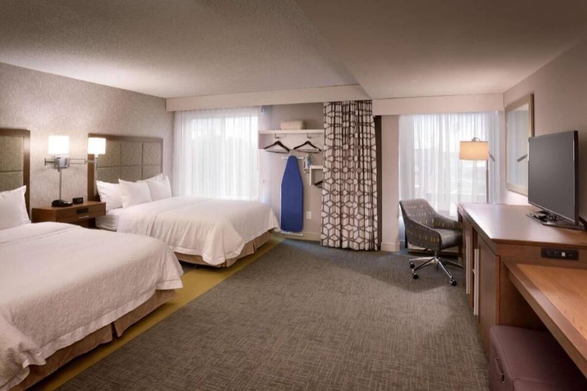A hotel room with two beds, a desk, a chair, a TV, and a shower area.