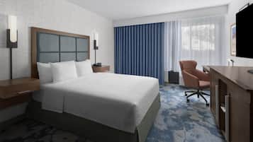 A hotel room with a large bed, a desk, a chair, a TV, and a window with curtains.