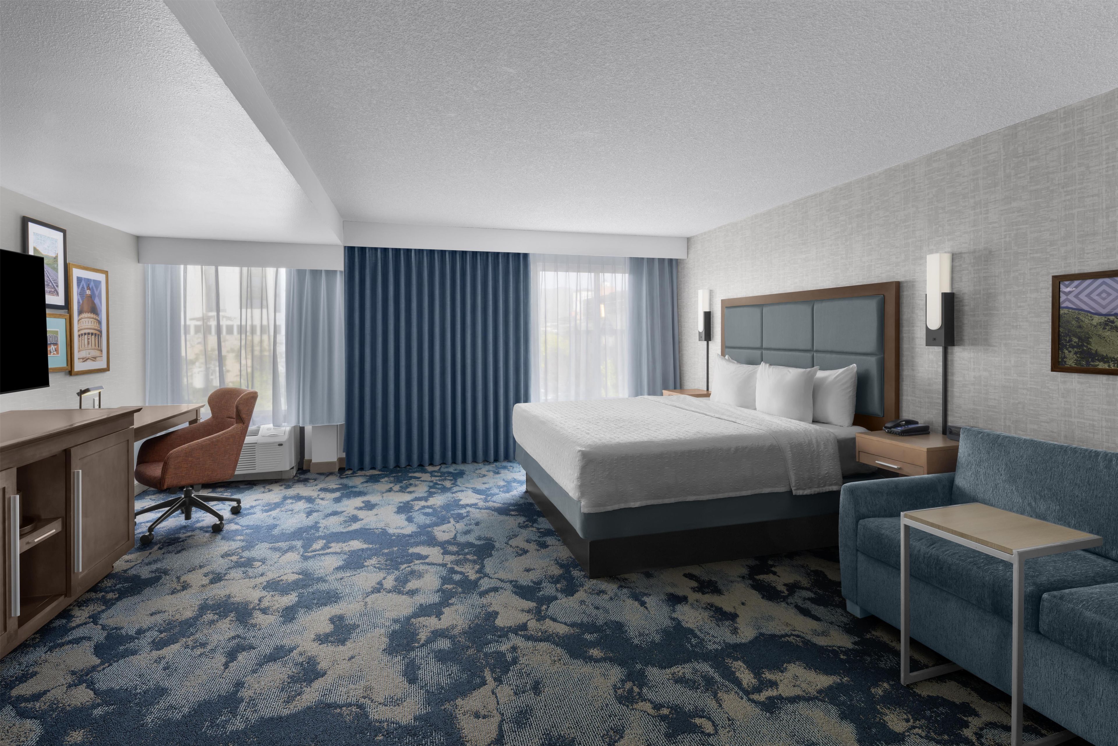 A hotel room with a bed, a desk, a chair, a sofa, and a TV.