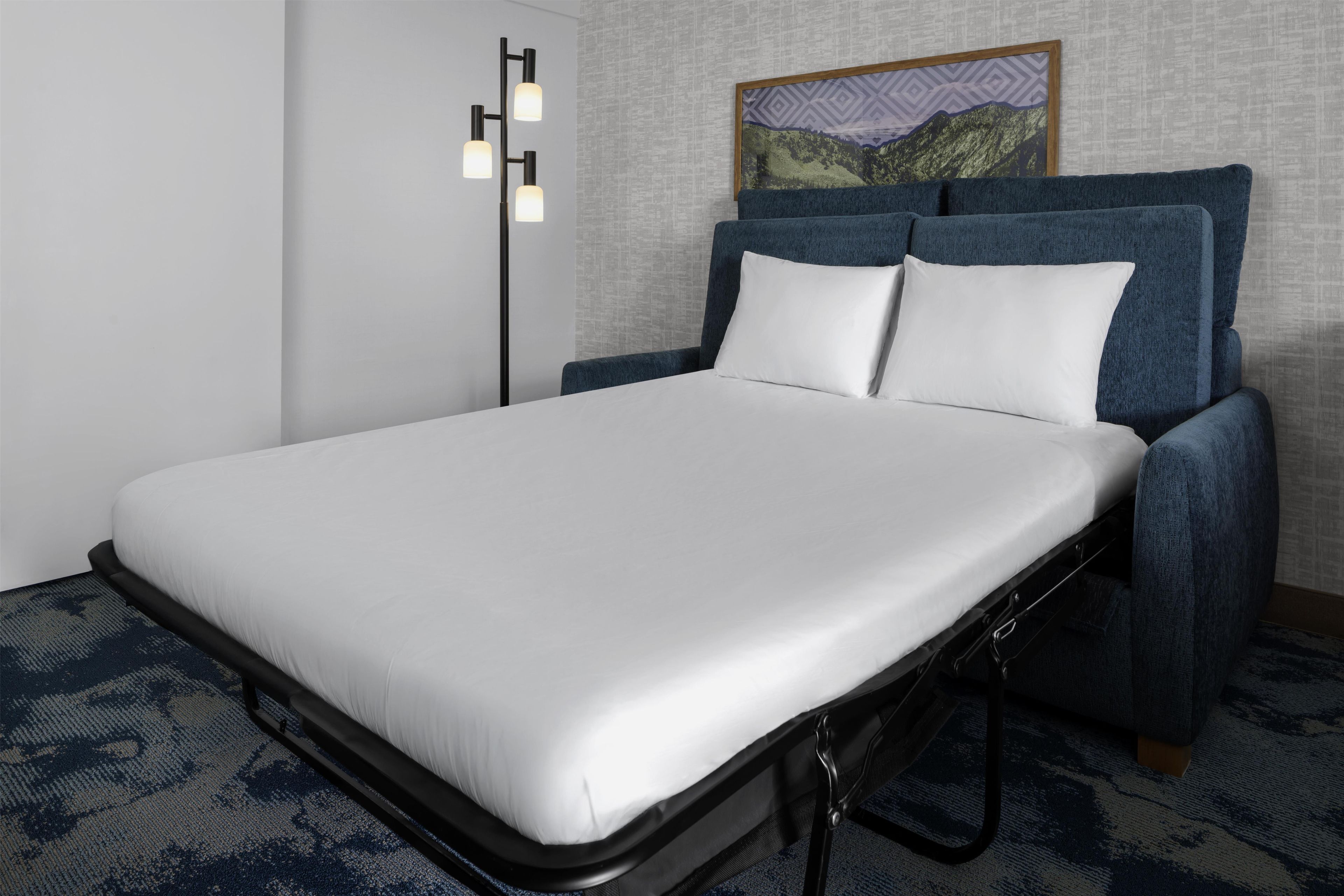 A single bed with a white mattress and a blue headboard in a hotel room.
