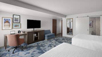 A hotel room with a bed, a desk with a chair, a television, and a large mirror.