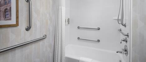 Un baño con bañera, barras de apoyo, ducha y toallero.