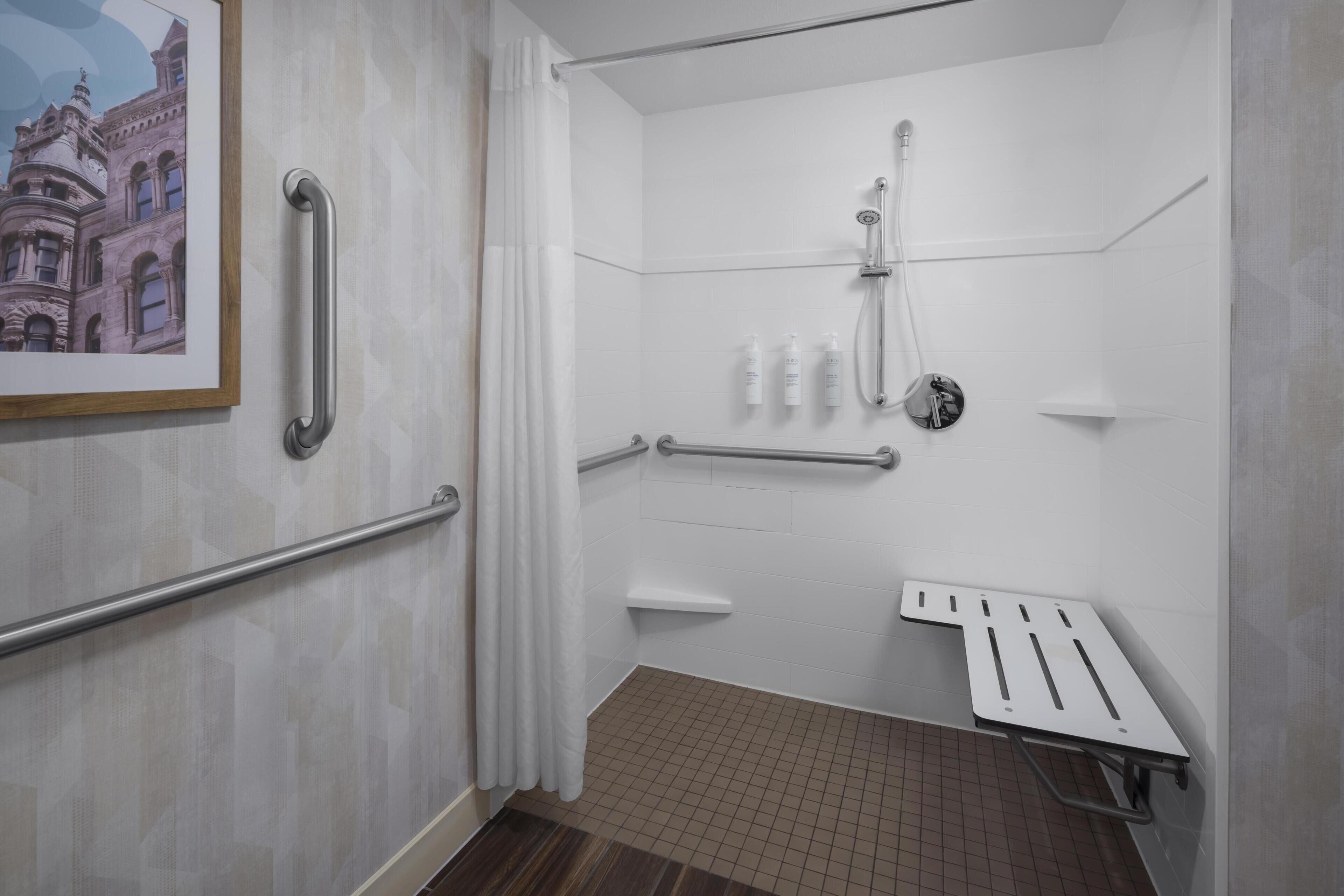 Douchekamer toegankelijk voor rolstoelen, met handgrepen, douchekop en een handrail.