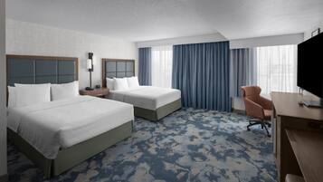 A hotel room with two beds, a desk, a chair, a TV, and a large window with curtains.
