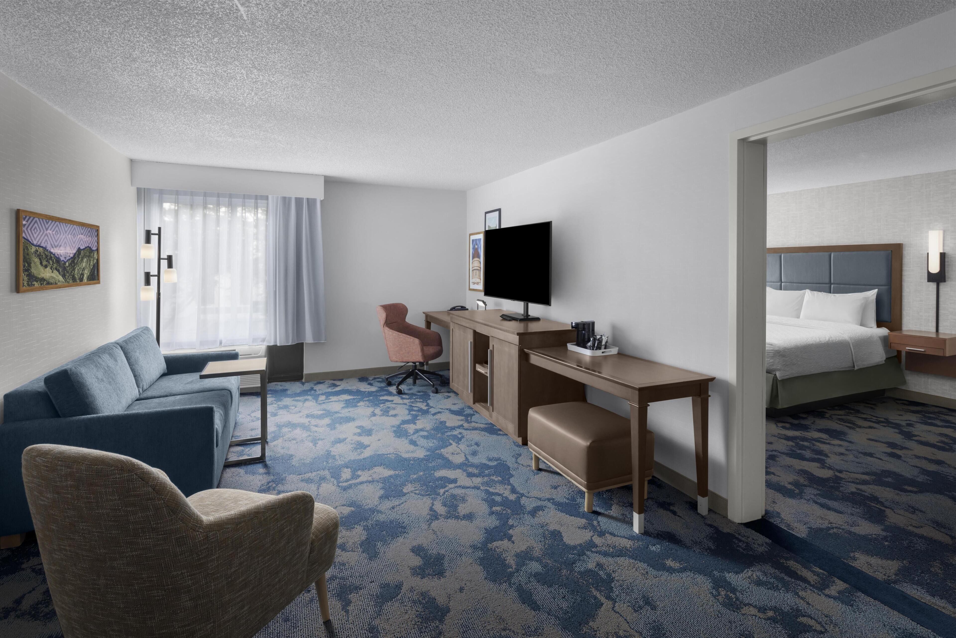 Hotellihuone, jossa on sohva, työpöytä, televisio, sänky ja tuoli.