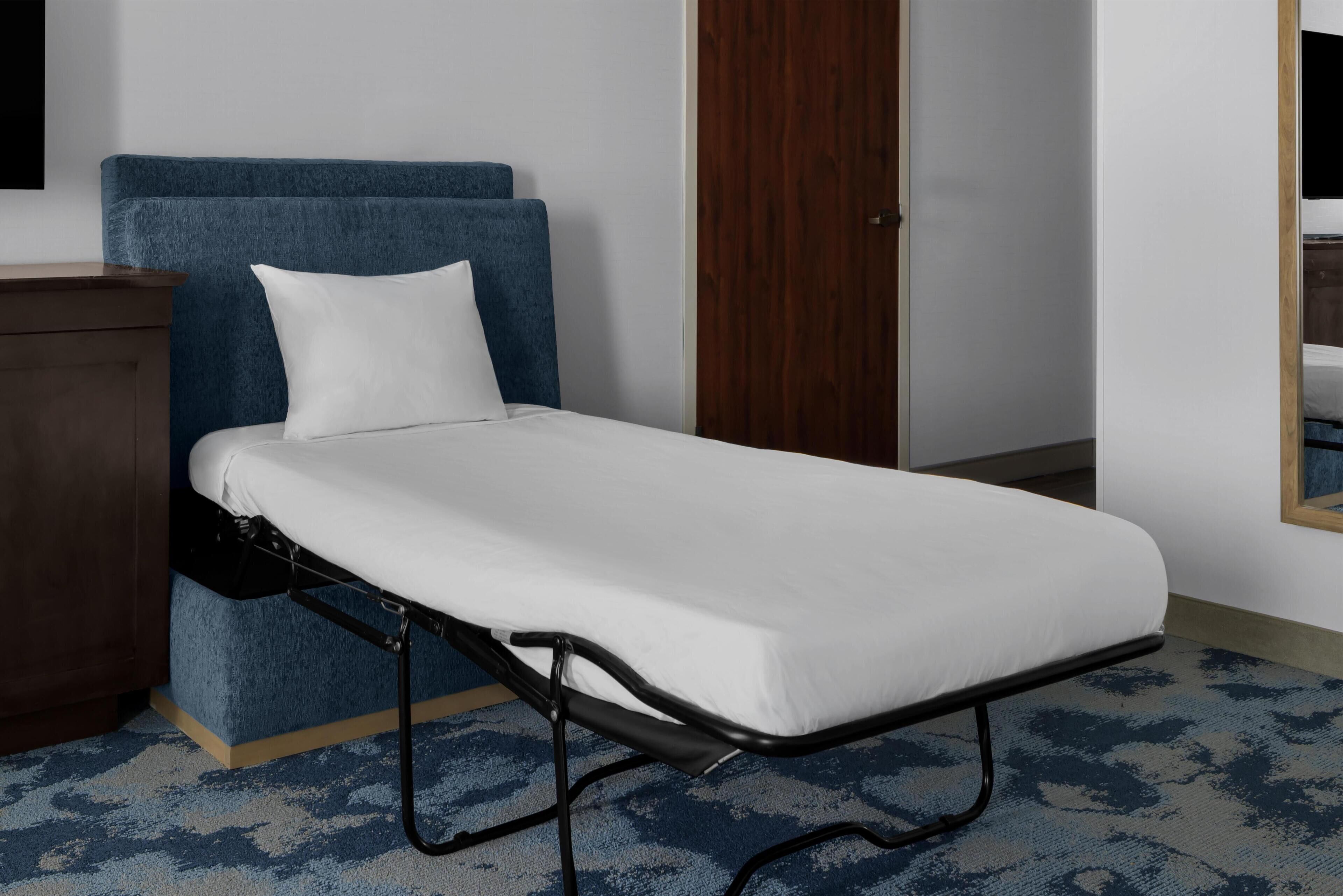 Una cama individual con colchón blanco y cabecera azul en una habitación con puerta de madera y alfombra azul.