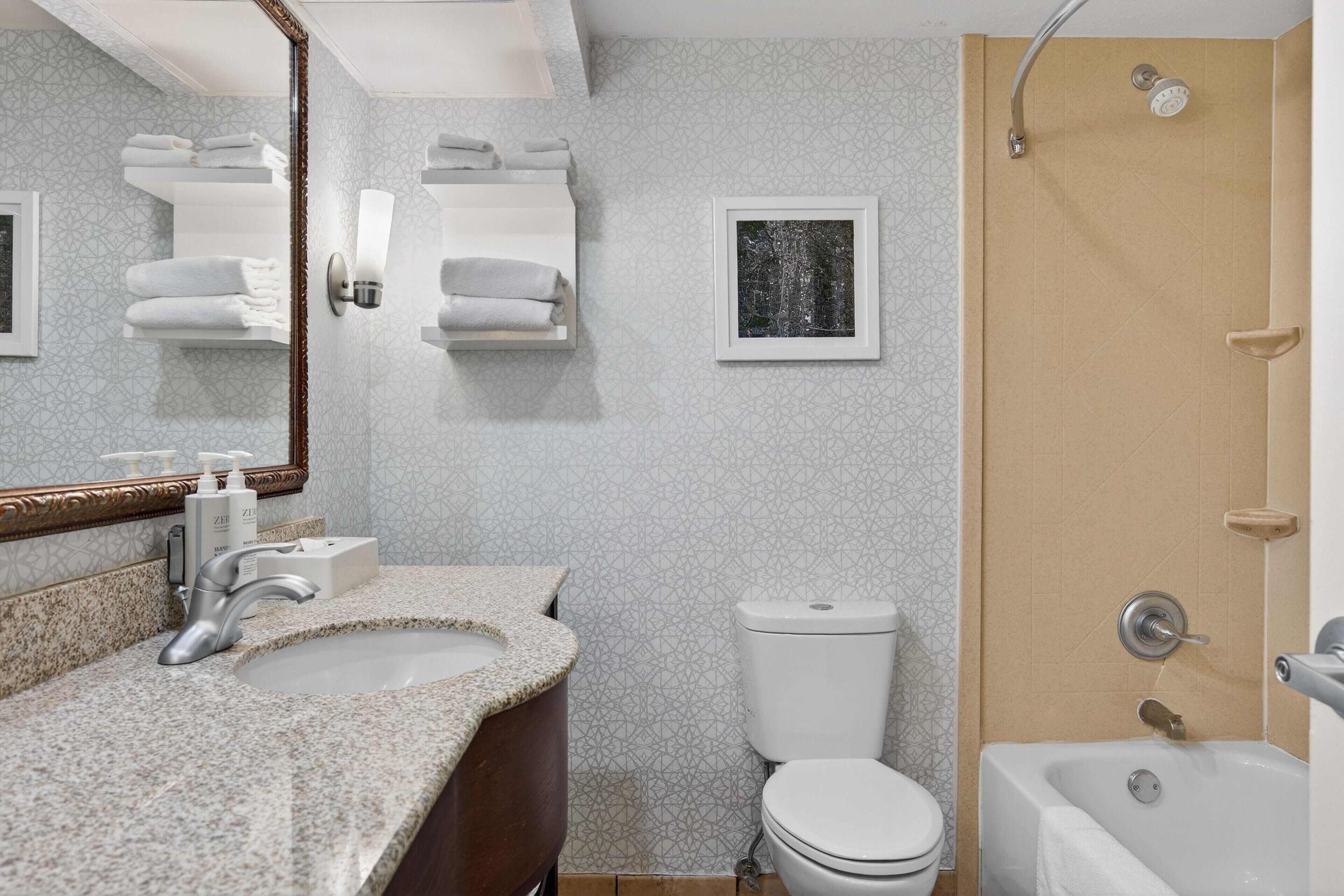 Une salle de bain avec un lavabo en granit, un miroir, des toilettes, une douche et un tableau encadré au mur.