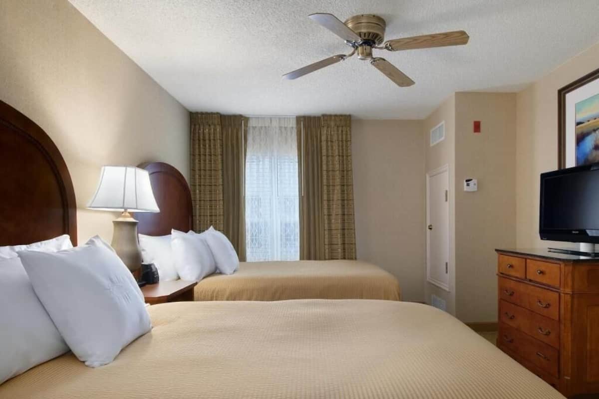 Ein Hotelzimmer mit zwei Betten, einem Deckenventilator, einem Fernseher und einer Kommode.