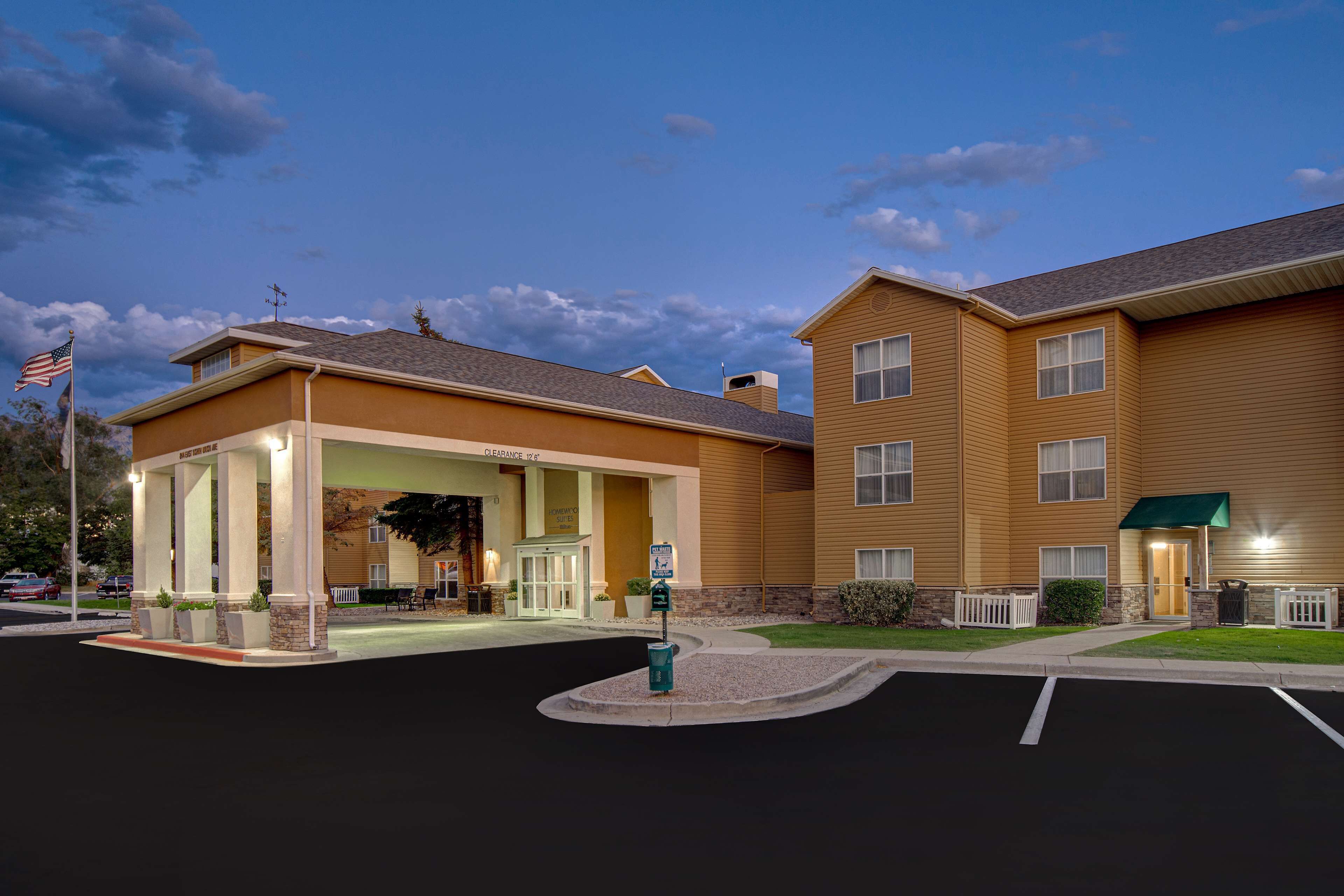 A hotel with a covered entrance, a parking lot, and a flag.