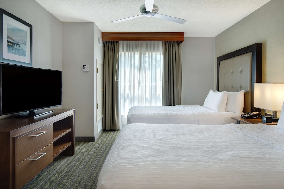 Ein Hotelzimmer mit zwei Betten, einem Flachbildfernseher, einer Holzkommode und einem Deckenventilator.