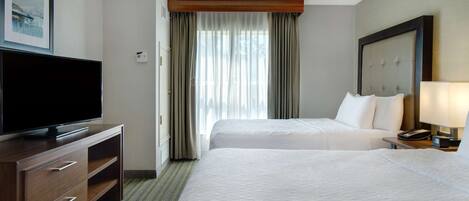A hotel room with two beds, a flat-screen TV, a wooden dresser, and a ceiling fan.