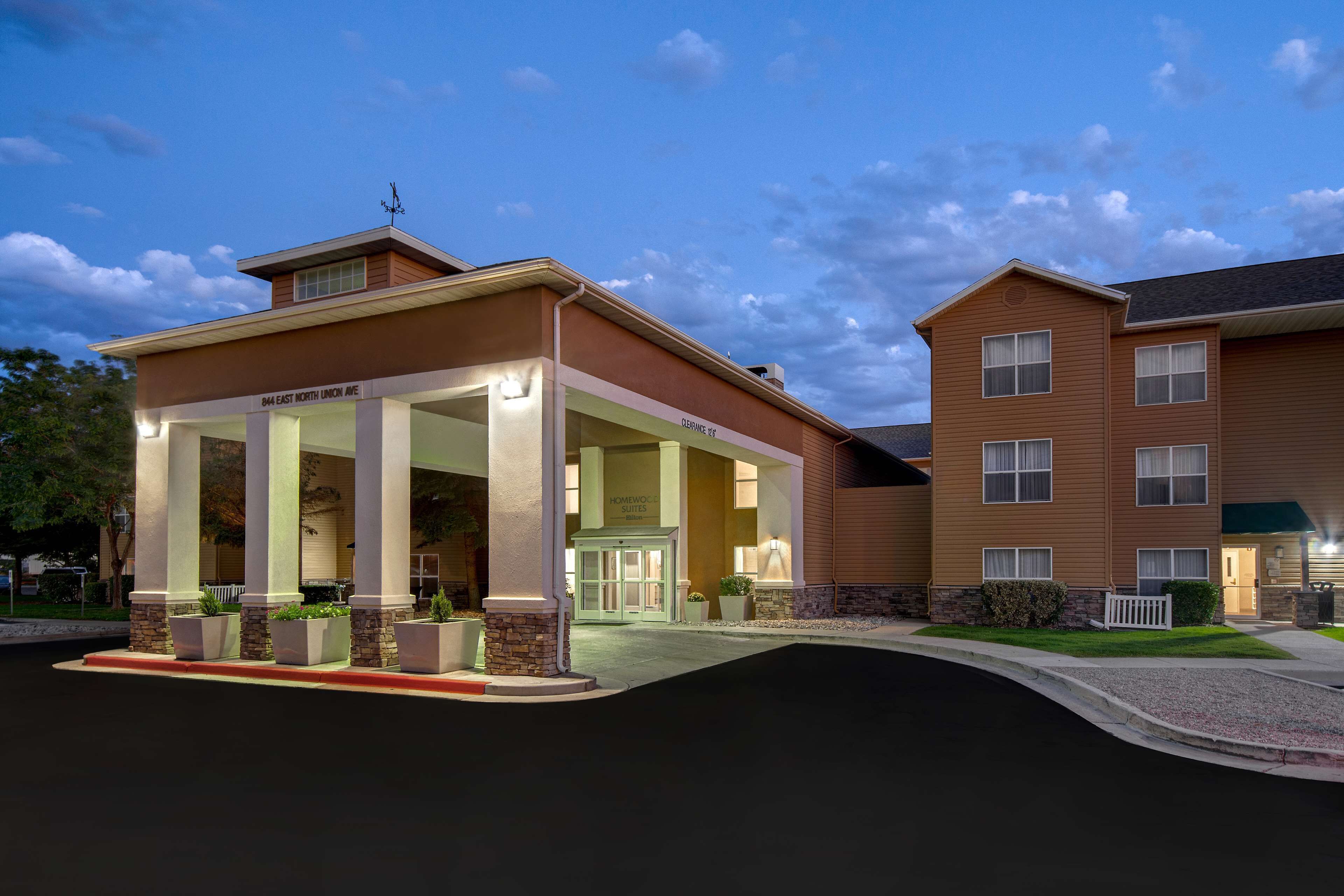 A hotel with a covered entrance, a sign for "Homewood Suites," and a well-lit facade.